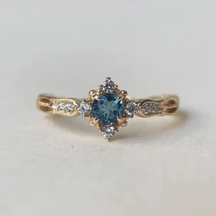 Swan Pırlanta London Blue Topaz tektaş yüzük, altın renkli ayar üzerinde mavi taş ve yanındaki parlak pırlantalarla zarif bir tasarım.